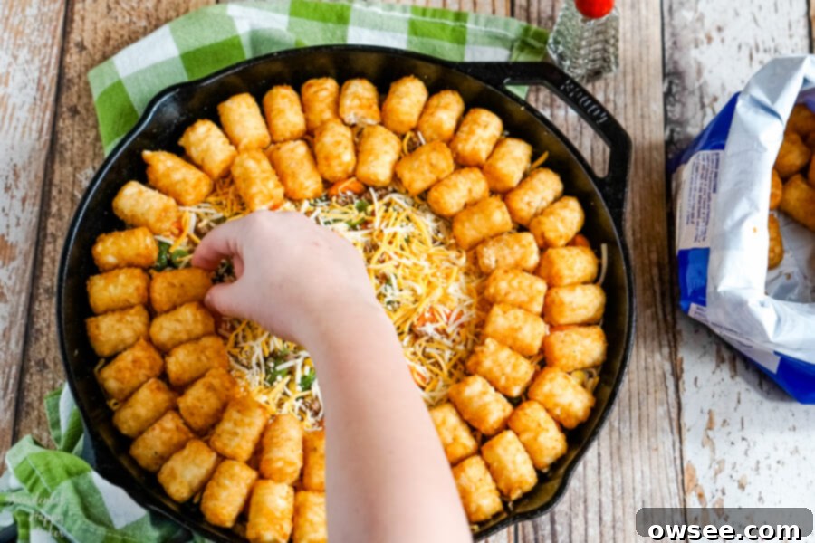 A layer of cheddar cheese is added before finishing the casserole with a layer of frozen tater tots. 