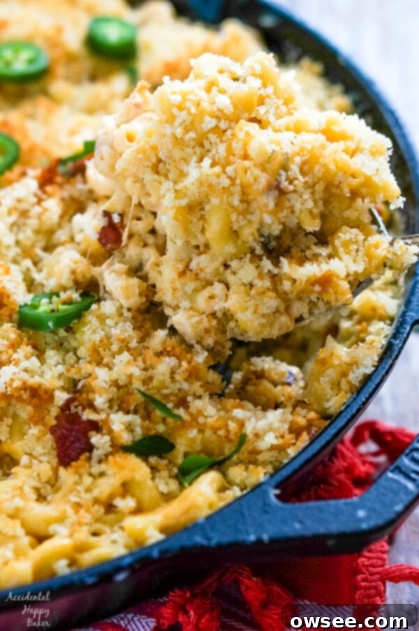 A serving of Jalapeno Bacon Mac and Cheese is removed from a cast iron skillet, showcasing the golden-brown topping and gooey interior.