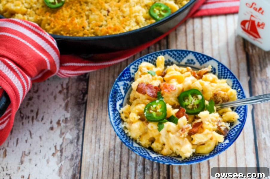 A blue and white bowl full of rich, creamy jalapeno bacon mac and cheese, served next to the cast iron skillet it was cooked in.