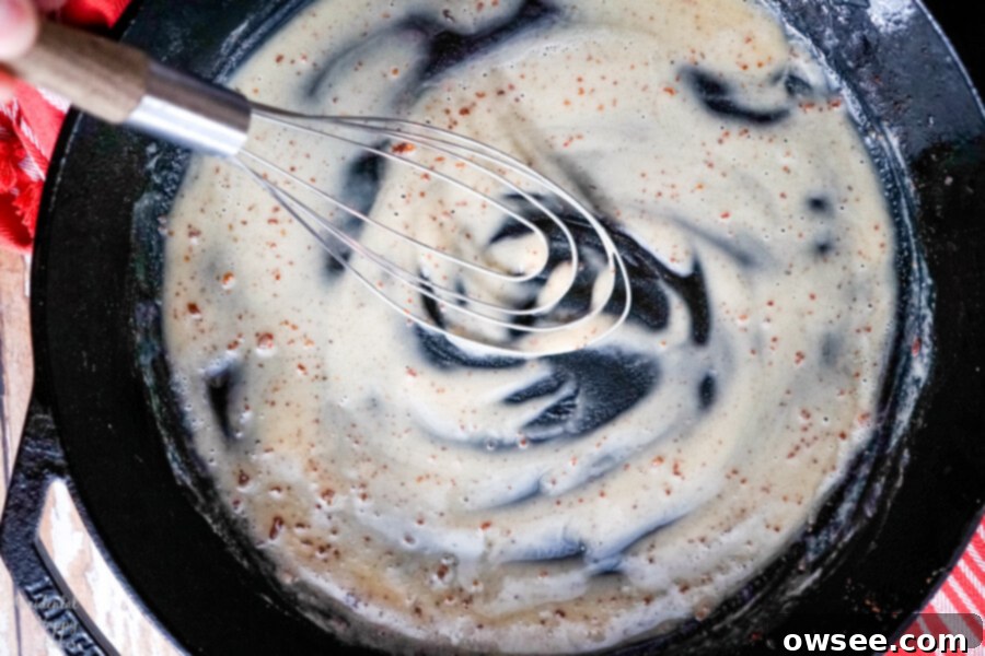 Flour is stirred into the hot bacon grease in a cast iron skillet to create a roux, the base for the creamy cheese sauce.