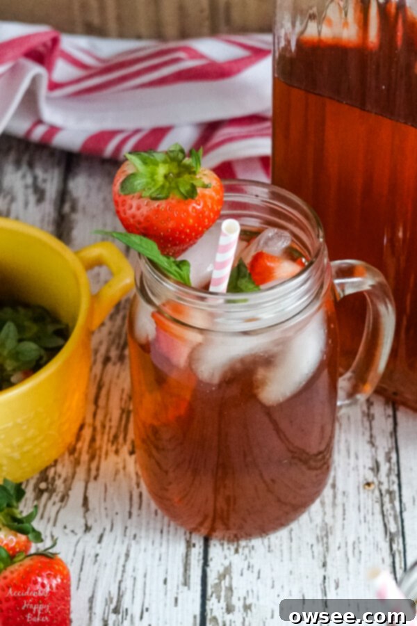 A mason jar cup of strawberry basil iced tea sitting next to a pitcher. 