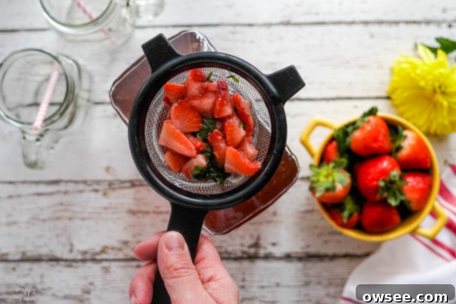 Straining the cooked strawberries and basil from the syrup using a fine mesh sieve. 