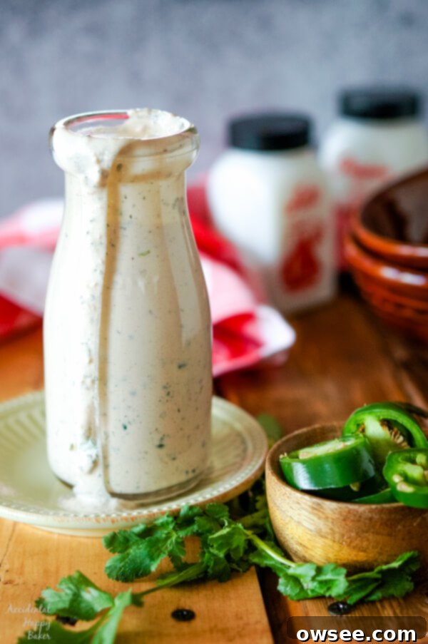 A bottle of creamy cilantro jalapeno ranch dressing with fresh cilantro sprigs and a bowl of sliced green jalapeno peppers on the side, highlighting the fresh ingredients.