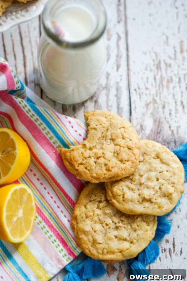 Lemon Cowboy Cookies 7 A beautifully arranged stack of golden-brown Lemon Cowboy Cookies resting delicately on a striped linen towel, with a refreshing bottle of milk positioned invitingly beside them, promising a delicious pairing.