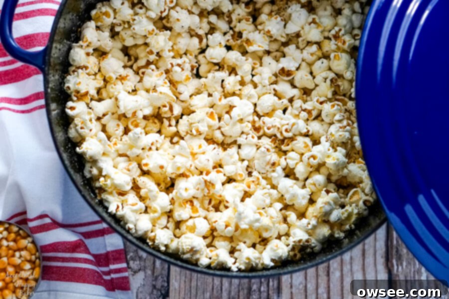 A vibrant blue Dutch oven overflowing with a generous amount of freshly popped golden popcorn, perfectly fluffy and inviting.