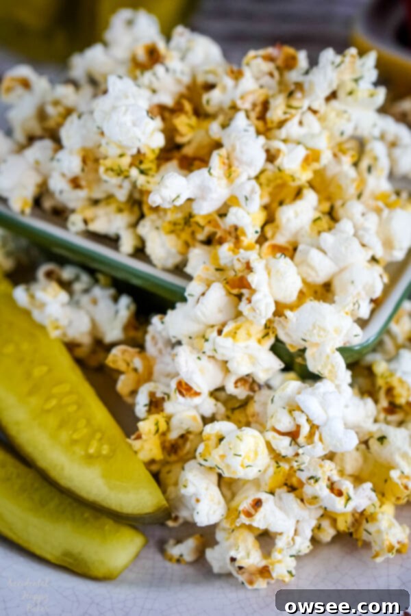 A bowl of dill pickle popcorn next to two dill pickle spears, showcasing the natural seasoning and real pickle inspiration.