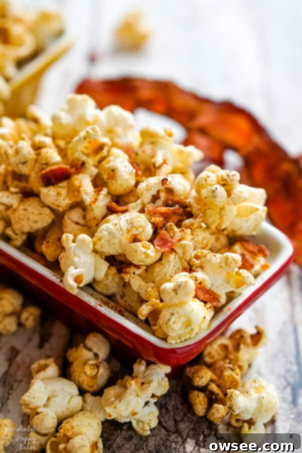 A vibrant red bowl filled to the brim with golden popcorn, garnished with several crispy strips of bacon in the background.