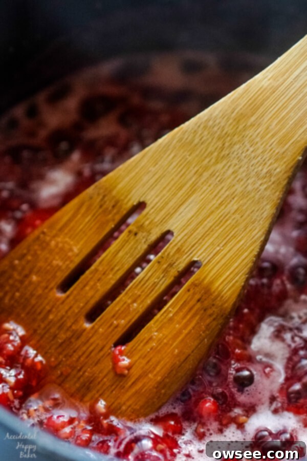 A close-up of fresh raspberries being mashed with a wooden spoon in a saucepan with simmering honey, creating a delicious berry reduction.