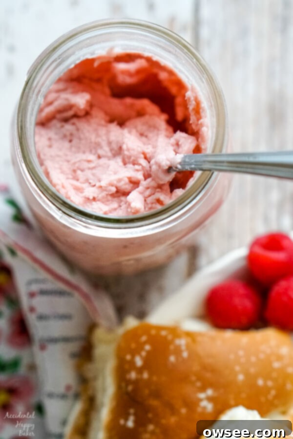 A close-up of a glass mason jar filled with the finished, creamy, and vibrant pink raspberry honey butter, ready for serving or storage.