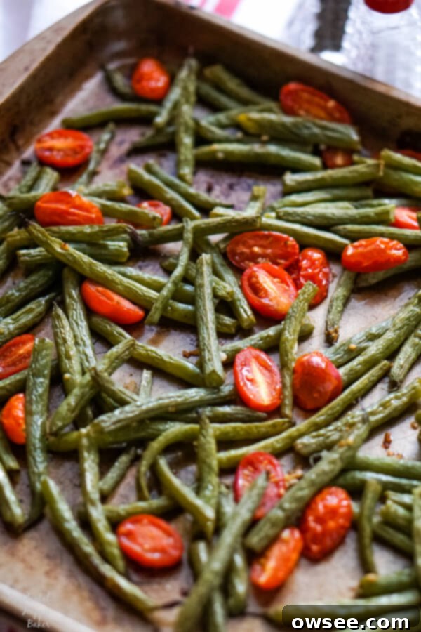 Green beans and cherry tomatoes on a sheet pan just after coming out of the oven. 
