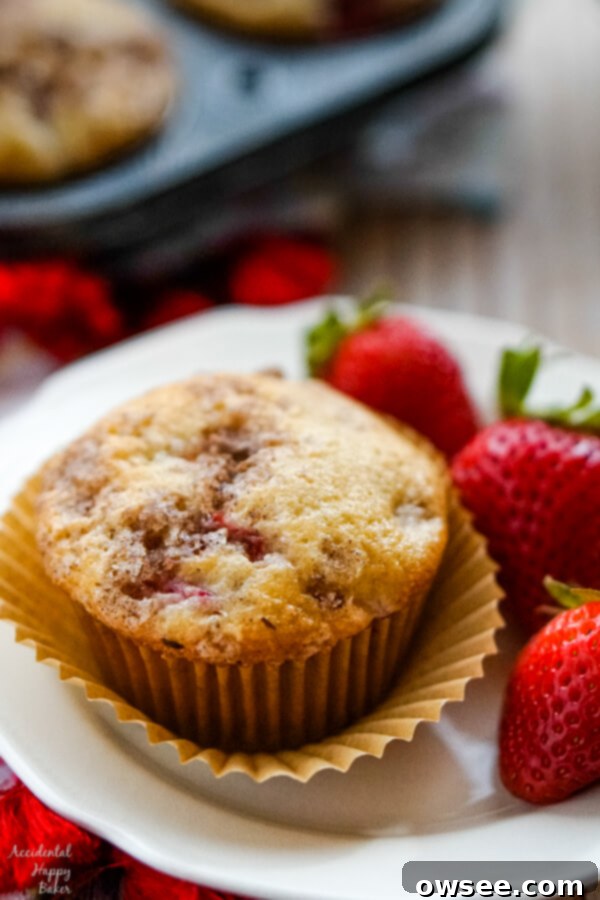 A strawberry rhubarb muffin on a plate with 3 strawberries.