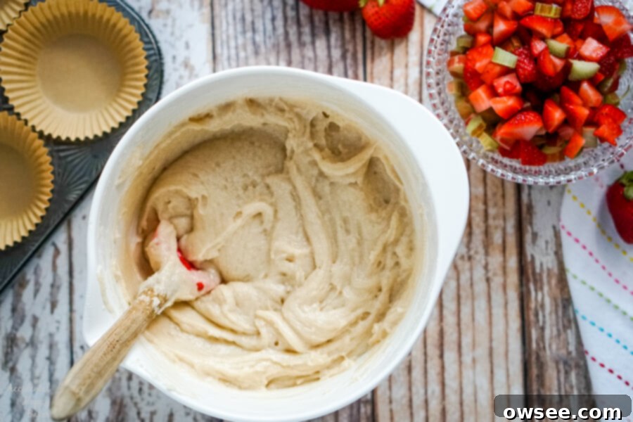 A white batter bowl full of muffin batter next to a bowl of chopped strawberries and rhubarb.
