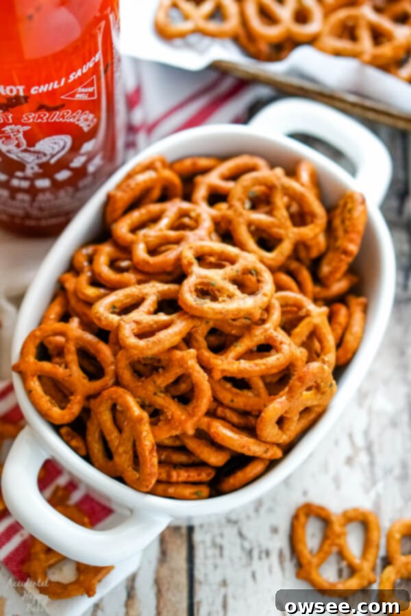 Kickin' Sriracha Ranch Pretzels 6 A white bowl full of spicy ranch pretzels next to a bottle of sriracha sauce.