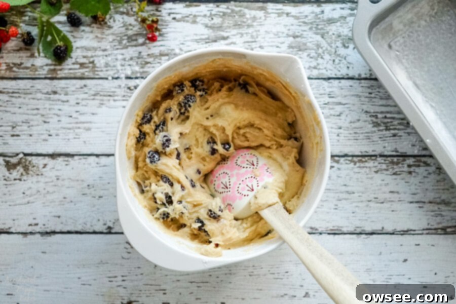 A large mixing bowl filled with creamy bread batter, beautifully speckled with vibrant, whole blackberries folded in, ready for baking.