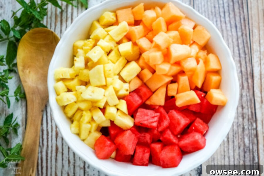 Sweet Watermelon Delight 3 A large white bowl filled with uniformly chopped watermelon, cantaloupe, and pineapple cubes, ready for the dressing and mint.