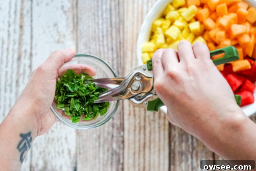 A person is using kitchen shears to finely chop fresh mint leaves into a small bowl, showcasing an easy method for herb preparation.