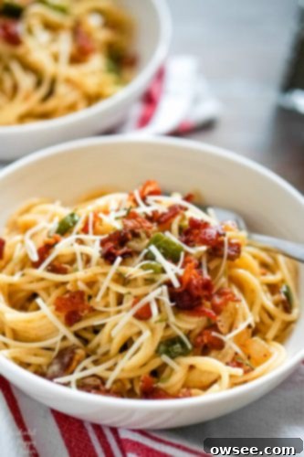 A white bowl full of spaghetti carbonara, garnished with fresh parsley and black pepper, ready to be enjoyed.