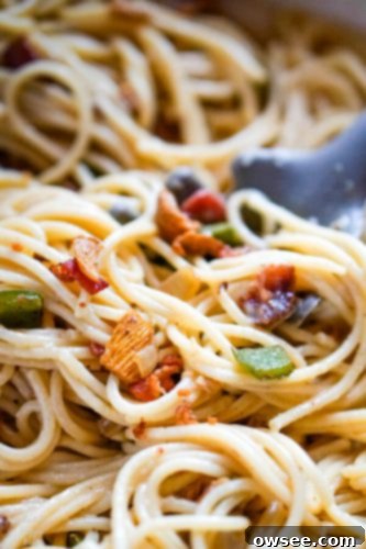 A large pan filled with freshly made spaghetti carbonara, with a serving utensil lifting a portion, showcasing the creamy sauce and crispy bacon bits.