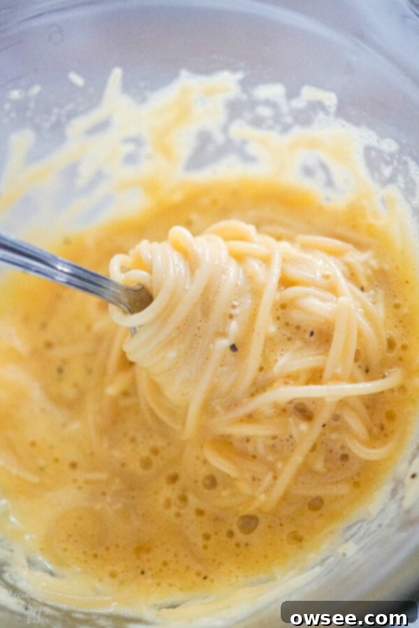 Steaming hot spaghetti is added to a bowl containing whisked eggs and cheese, then quickly tossed to temper the eggs.