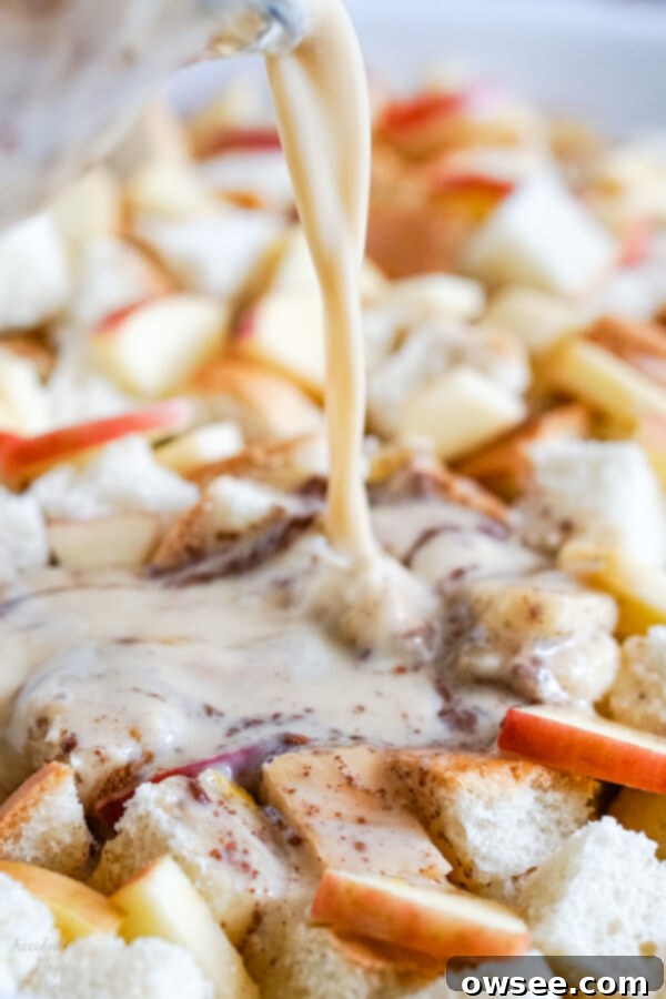 A close-up image showing the creamy milk and egg mixture being poured evenly over the layers of bread and apples in the casserole dish.