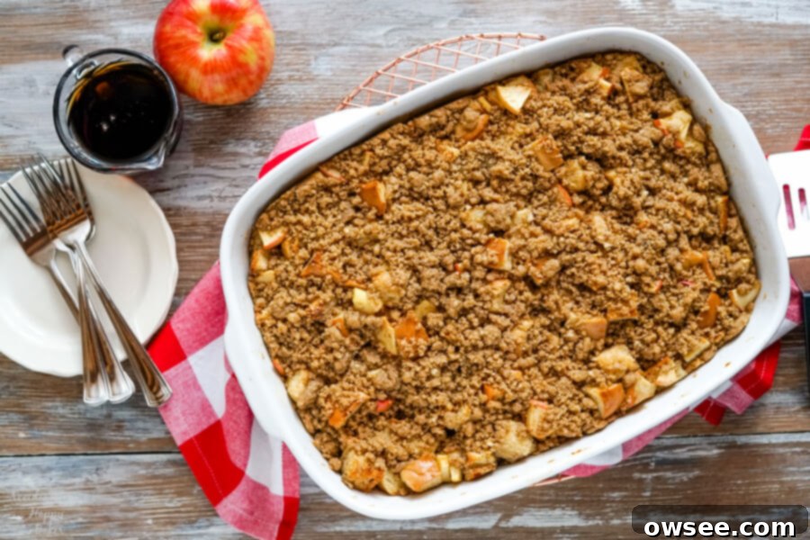 A freshly baked pan of Cinnamon Apple French Toast Casserole, golden brown and topped with streusel, resting on a rustic red checked towel.
