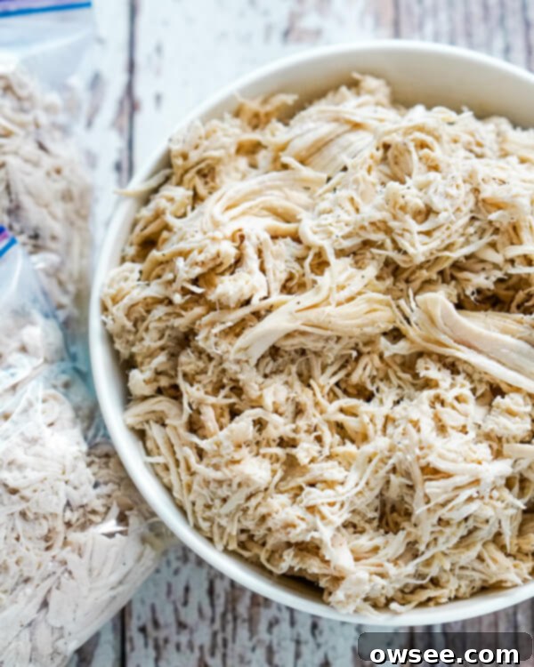 The Ultimate Big Batch Instant Pot Shredded Chicken 10 A white bowl full of shredded chicken with 2 freezer bags of chicken next to it.