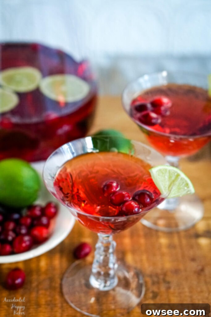 Sparkling Cranberry Moscato Punch 2 A sparkling glass of cranberry moscato punch garnished with fresh cranberries and lime, sitting on a wooden serving tray, ready for a party.