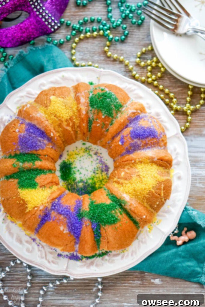 Effortless King Cake Celebration 2 A white plate holding a king cake made from crescent rolls on a table spread with Mardi Gras beads.