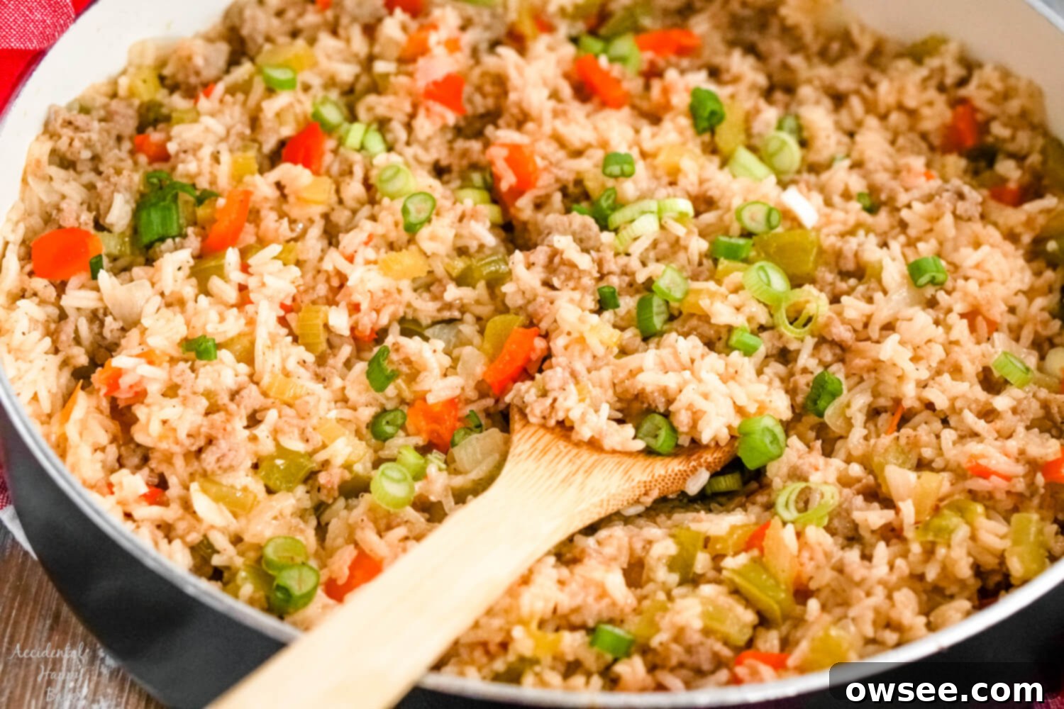 Savory Sausage Dirty Rice 8 A skillet full of dirty rice with sausage with a wooden spoon holding a scoop of rice.