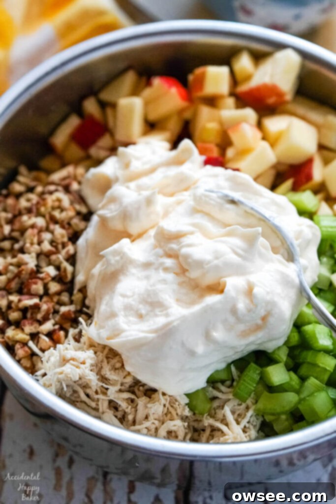 A mix of chopped pecans, diced apples, finely chopped celery, and creamy mayonnaise, all in a metal bowl, ready to be folded into chicken salad.