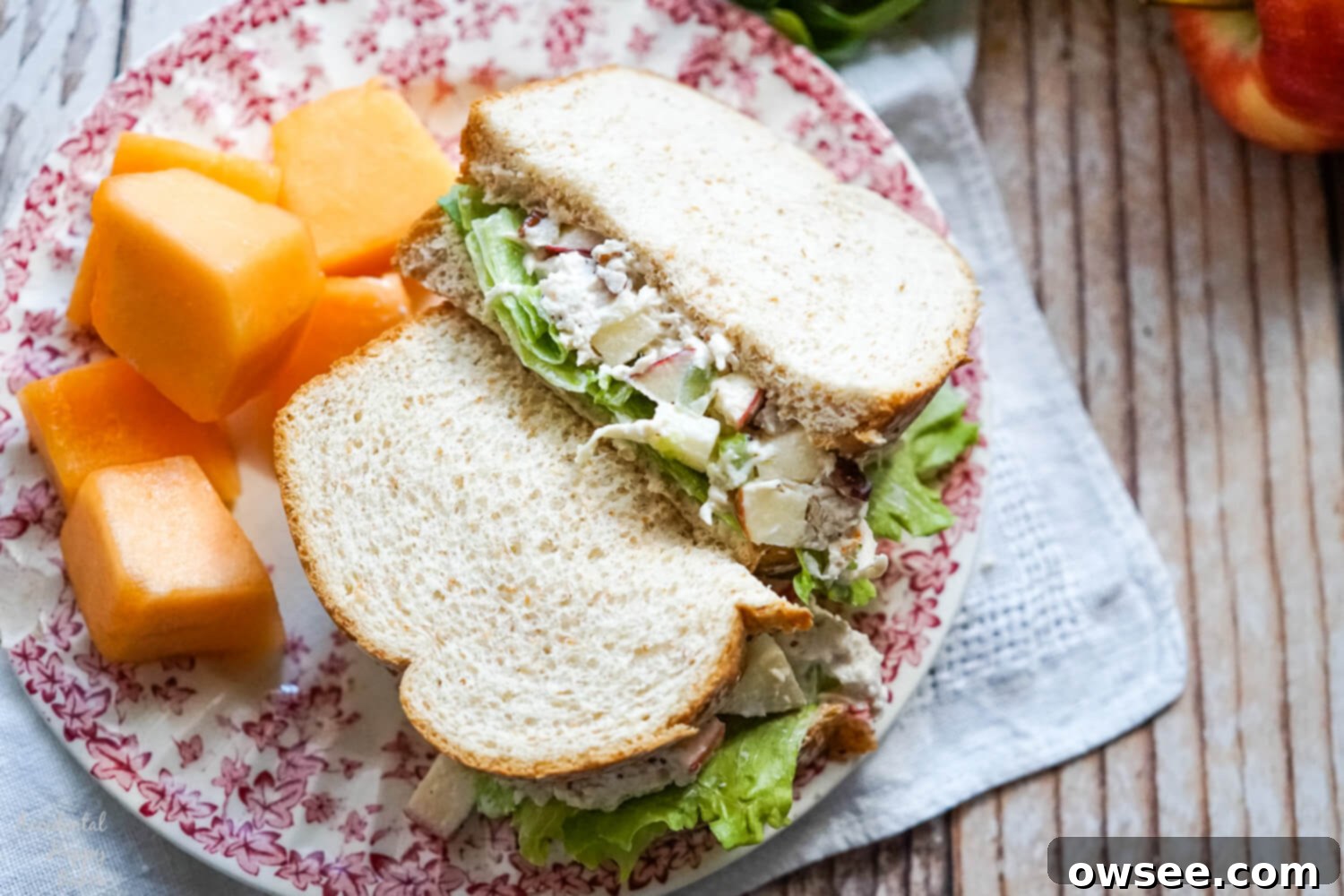 A vibrant apple pecan chicken salad sandwich with a side of fresh fruit, artfully arranged on a floral plate.