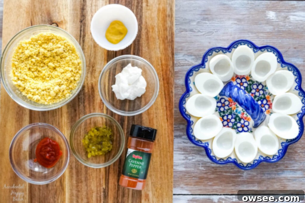 Ingredients for spicy deviled eggs in separate bowls on a cutting board, next to cooked egg whites in a deviled egg dish.