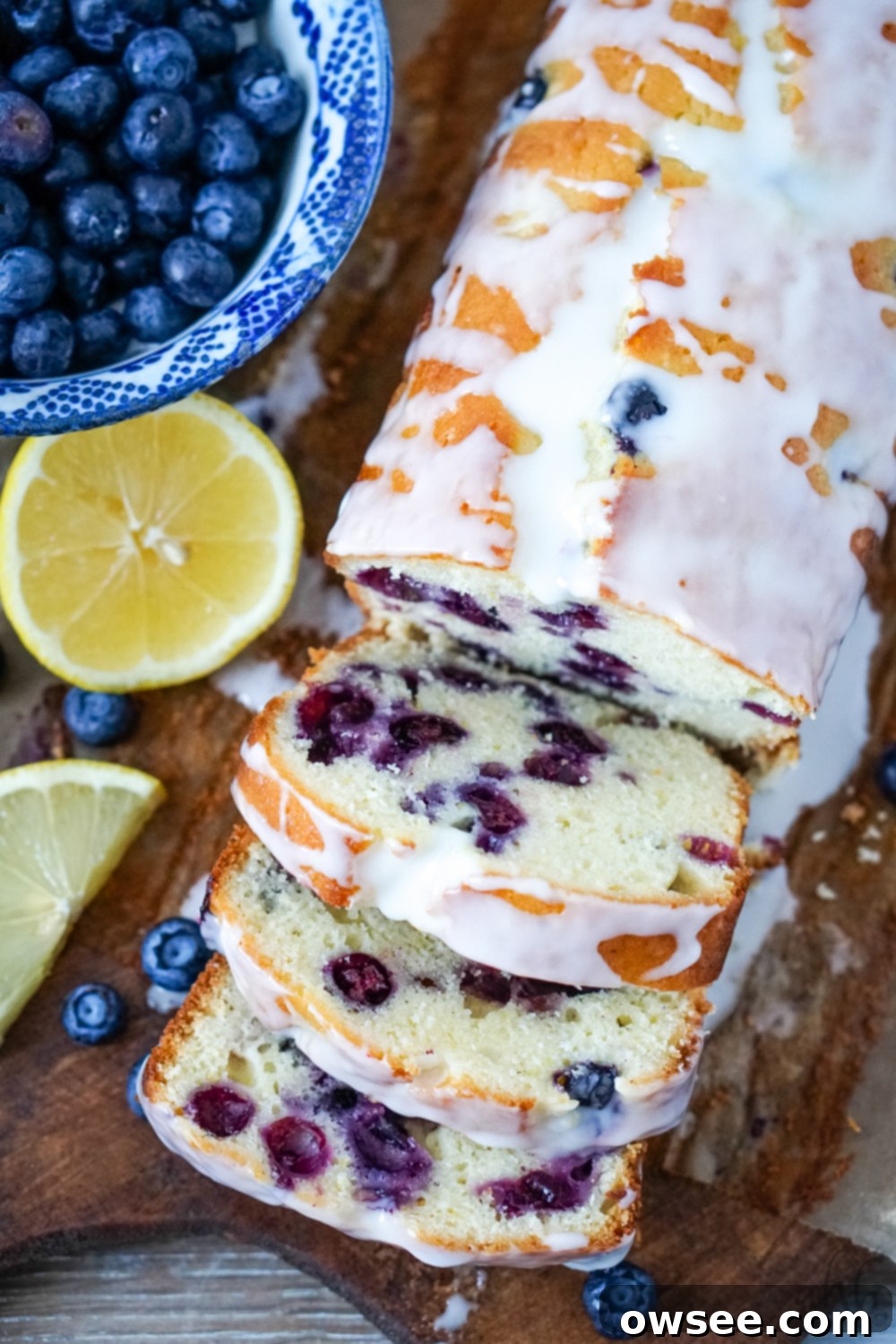 Zesty Lemon Blueberry Bread Drizzled with Buttermilk Glaze 2 A sliced loaf of lemon blueberry bread with buttermilk glaze over the top on a bread board with sliced lemons and a bowl of blueberries to one side. This moist quick bread is perfect for breakfast, brunch, or dessert.