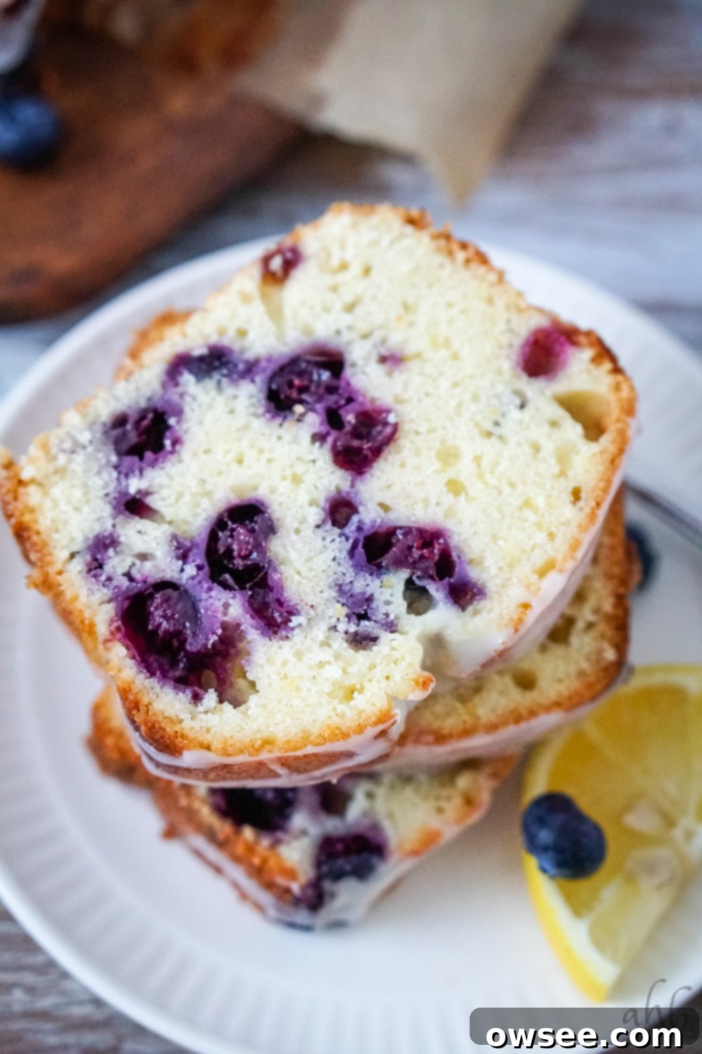 Zesty Lemon Blueberry Bread Drizzled with Buttermilk Glaze 3 Several slices of moist lemon blueberry buttermilk bread on a white plate with a fresh lemon slice. The bread is generously studded with blueberries and topped with a tangy buttermilk glaze.