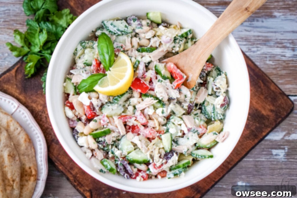 Creamy Mediterranean Tuna Salad 2 A red bowl of Mediterranean Tuna salad with a stack of pitas to one side, showcasing fresh vegetables and creamy dressing.