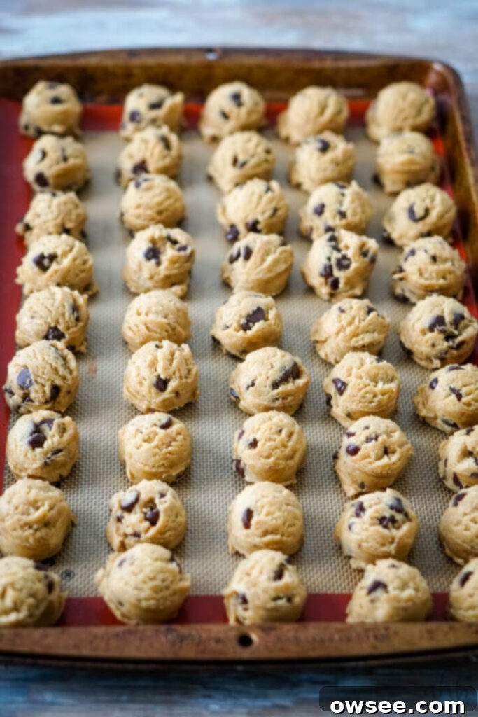 Scooped chocolate chip cookie dough balls neatly arranged on a parchment-lined baking sheet, ready for flash freezing.