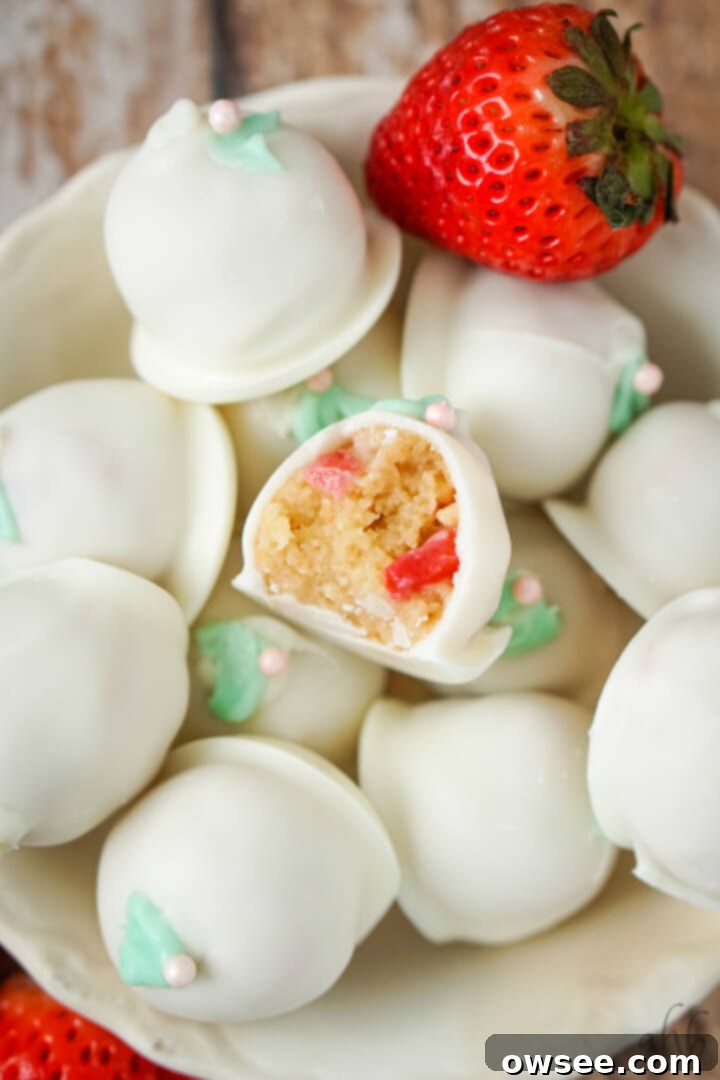 Easy Strawberry Cheesecake Truffles 10 A bowl full of strawberry cheesecake truffles with 2 fresh strawberries to the side.