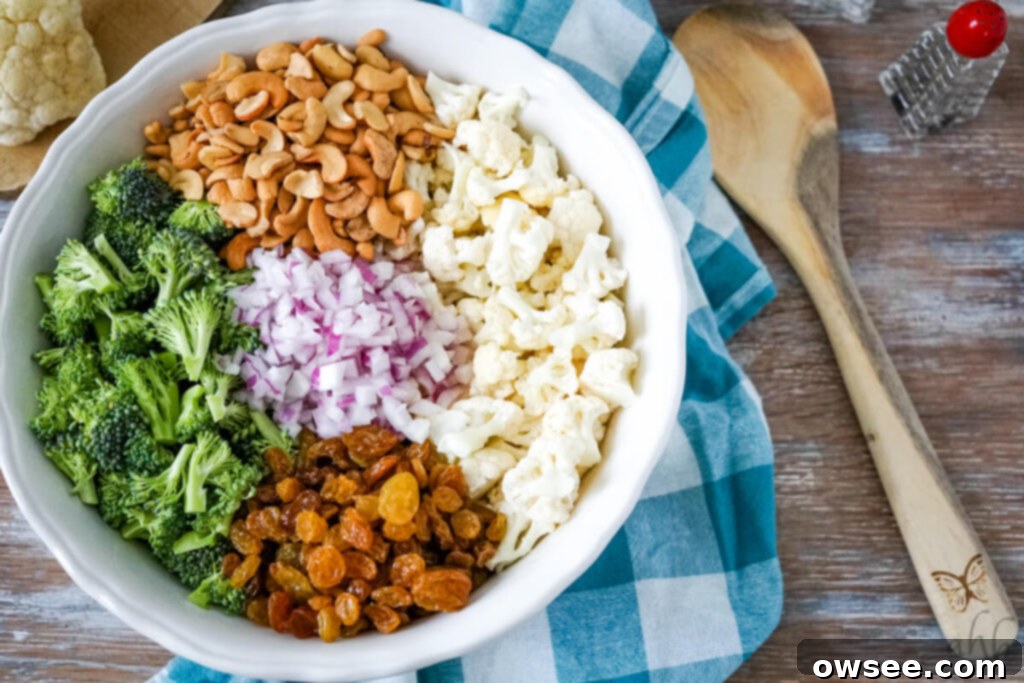 Creamy Amish Broccoli Cauliflower Medley 4 A large white bowl full of chopped broccoli, cashews, cauliflower, golden raisins, and red onions.