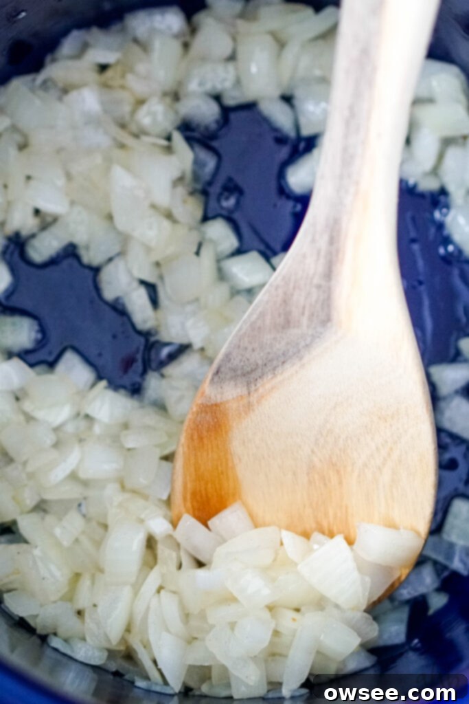 Effortless Four-Ingredient Potato Soup 6 Diced onion sautéing in bacon grease being stirred by a wooden spoon in a blue stockpot.