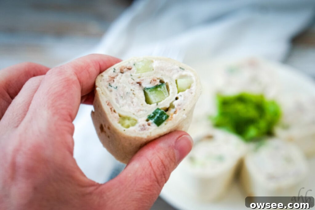 Tuna Roll-Ups 2 A plate of fresh tuna pinwheels arranged decoratively, showcasing their spiral pattern and creamy filling with visible cucumber pieces on a white plate with a dark background.