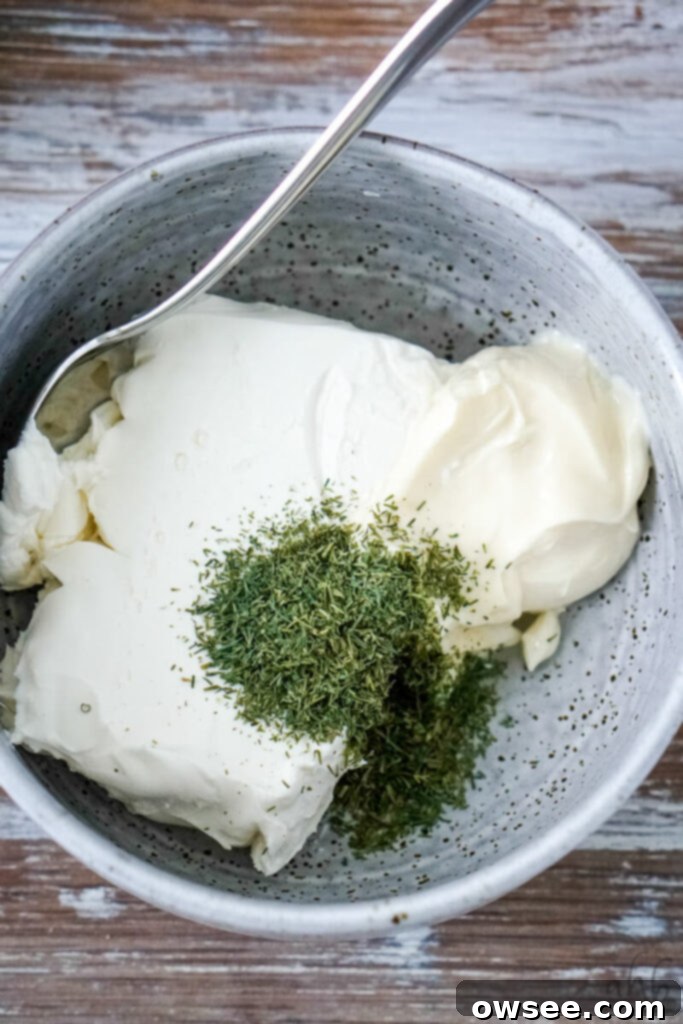 Tuna Roll-Ups 6 Cream cheese, mayonnaise, and fresh dill weed are being thoroughly mixed together with a spoon in a sleek gray mixing bowl.