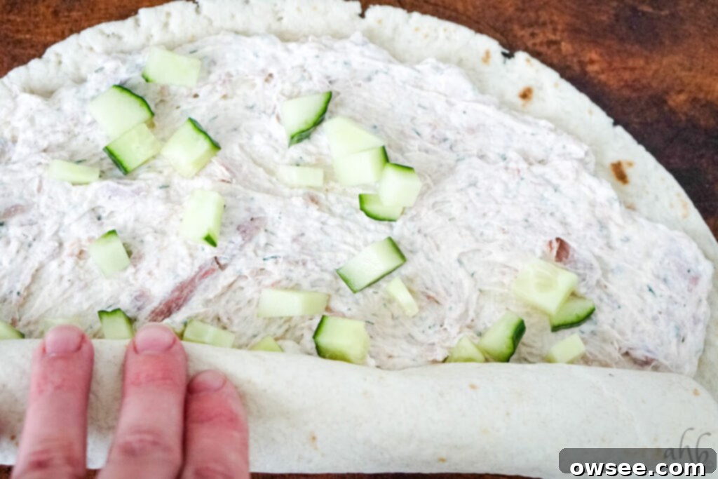 Tuna Roll-Ups 9 A flour tortilla, fully covered with tuna and cucumber filling, is being tightly rolled from one end to the other, creating a compact cylinder.