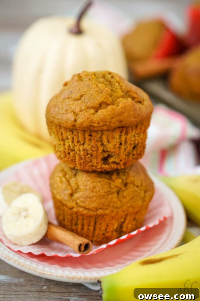 Golden Spiced Banana Pumpkin Muffins 4 A delicious pumpkin banana muffin, unwrapped, stacked on another, with slices of fresh banana and cinnamon sticks artfully arranged around them, ready to be enjoyed.