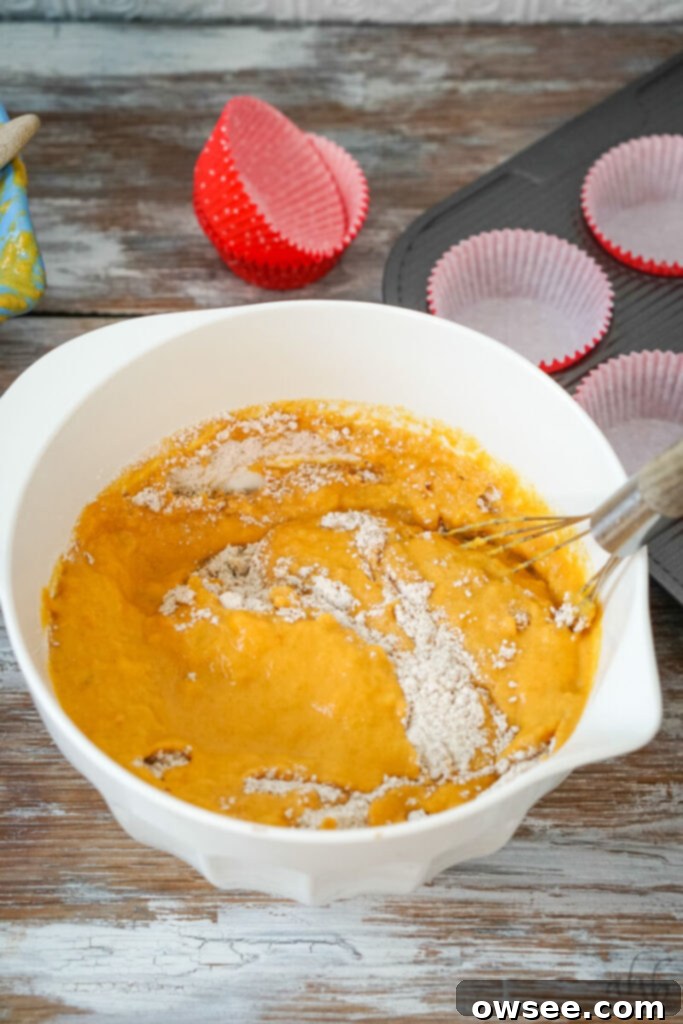 Golden Spiced Banana Pumpkin Muffins 7 The smooth wet ingredients are carefully poured into a well created in the center of the dry ingredients in a white mixing bowl. The mixture is then gently whisked until just moistened, taking care not to overmix.