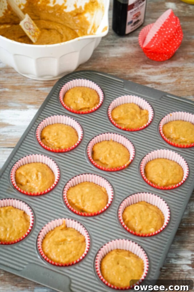 Golden Spiced Banana Pumpkin Muffins 8 The golden-brown muffin batter is evenly distributed into twelve muffin cups, each lined with a paper baking liner, ready for baking.