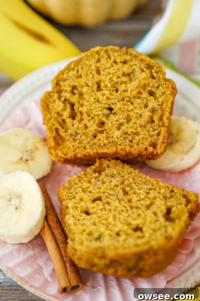 Golden Spiced Banana Pumpkin Muffins 9 A freshly baked pumpkin banana muffin, unwrapped and cut in half, showcasing its moist, fluffy interior. It's beautifully arranged next to slices of ripe banana and aromatic cinnamon sticks, highlighting its key ingredients and deliciousness.