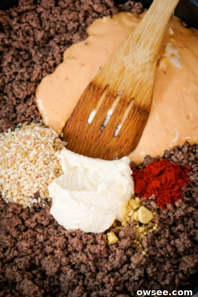 Big Mac Tater Tot Bake 7 A wooden spoon combines browned ground beef, thousand island dressing, dried minced onion, mayo, dried ground mustard, and paprika.