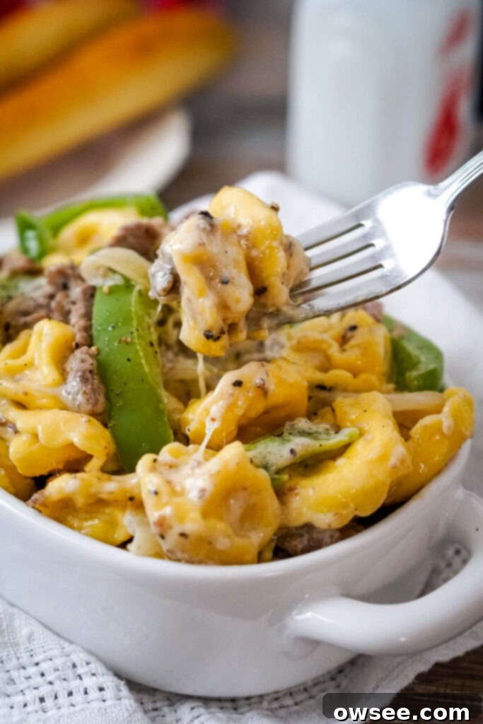 Philly Cheesesteak Filled Tortellini 2 A serving of Philly Cheesesteak Tortellini in a white dish being served with a fork, showcasing the creamy sauce, steak, peppers, and tortellini.