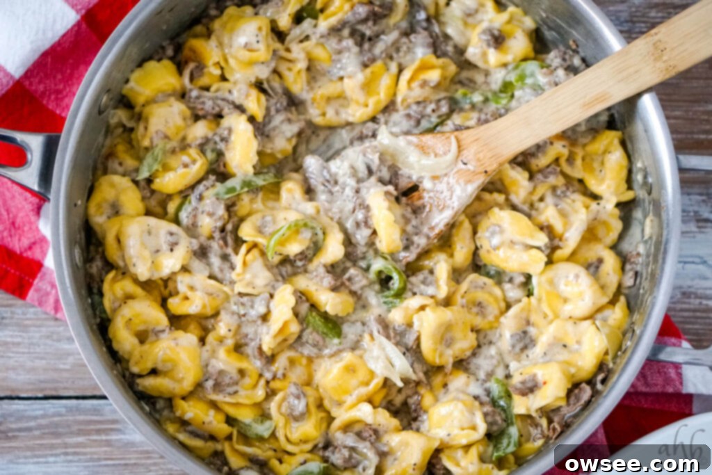 Philly Cheesesteak Filled Tortellini 8 A wooden spoon sits in the sauté pan with the creamy, cheesy Philly Cheesesteak Tortellini, ready to be served.